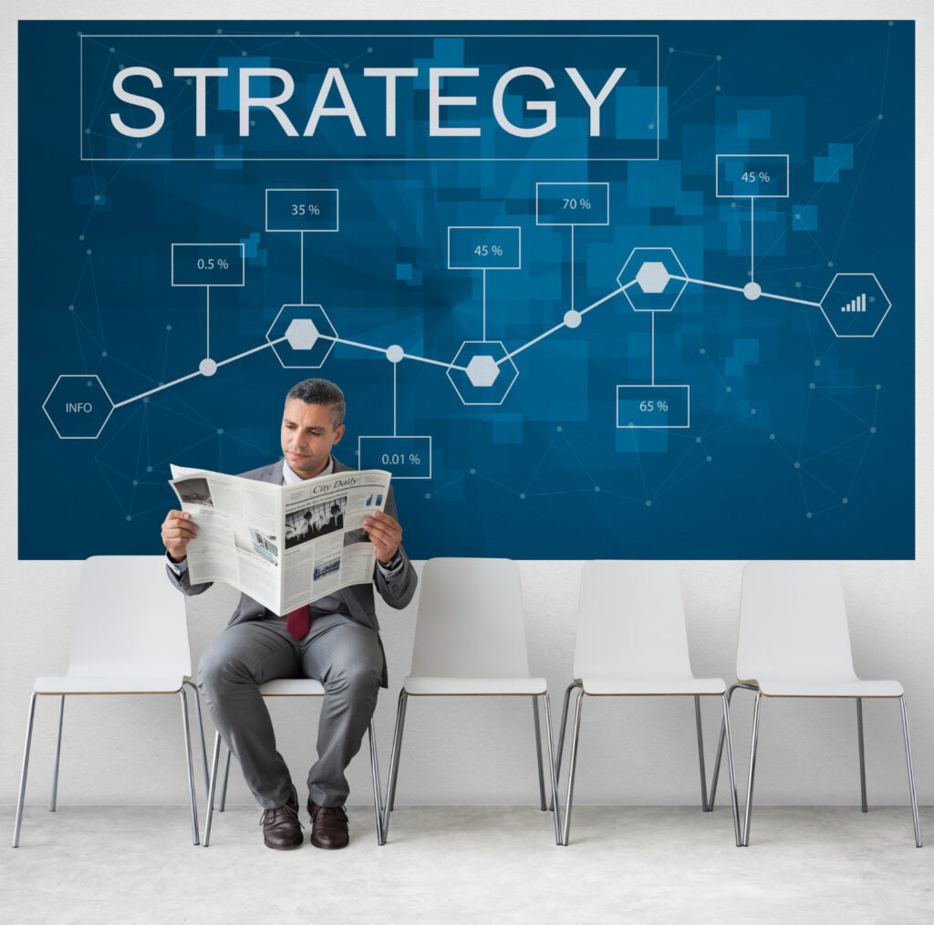 A businessman analyzes business strategy from a newspaper, positioned in front of a wall featuring a strategy diagram